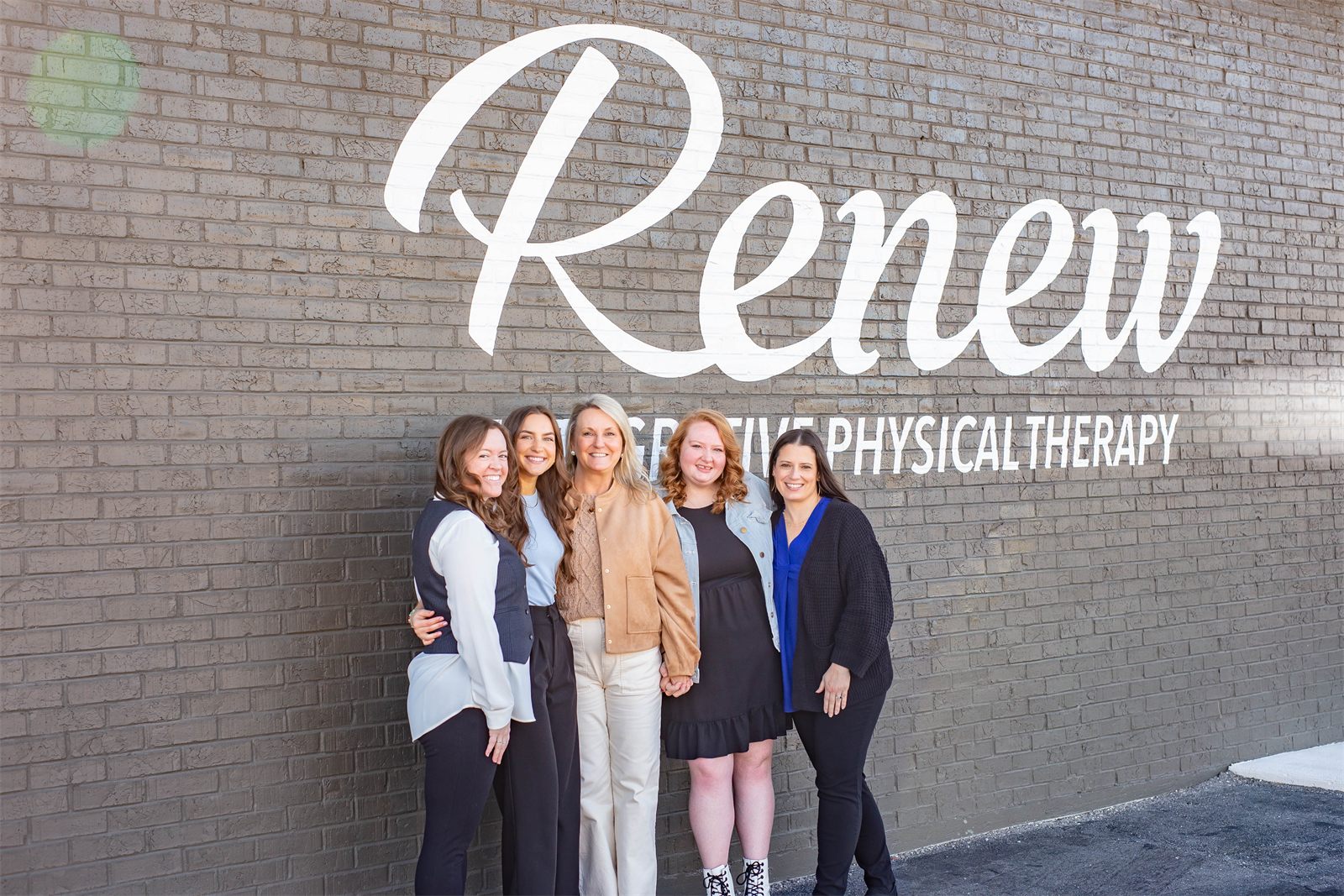 Renew's admin team in front of the Renew Integrative Physical Therapy wall sign